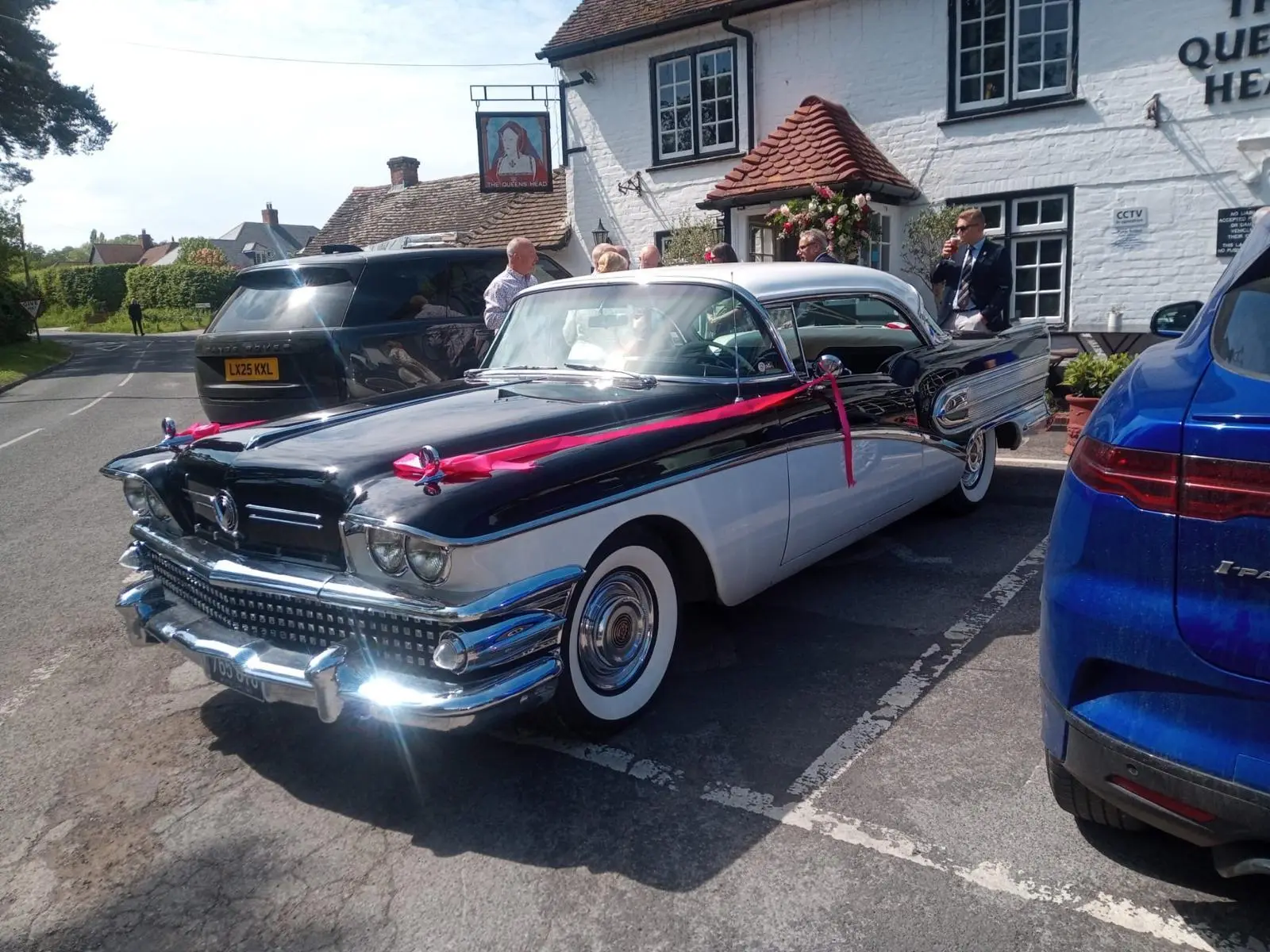 Classic black and white wedding car tied with pink ribbon outside The Queens Head